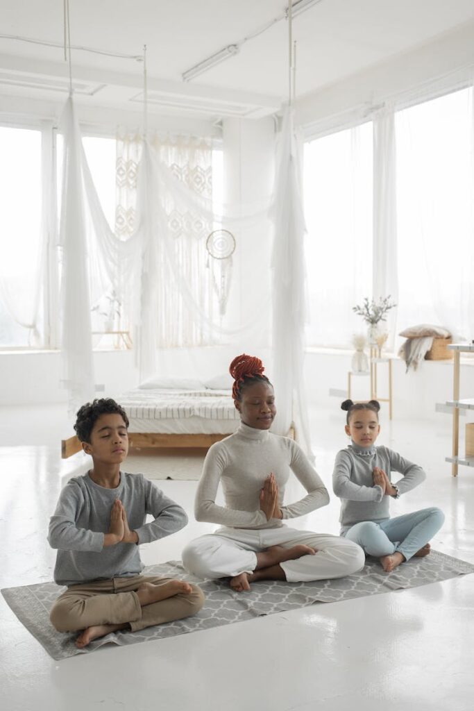 Young ethnic mother with cute children practicing yoga together at home